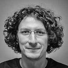 A headshot of a man with curly hair and glasses.