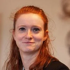 A headshot of a red-haired woman smiling at the camera.